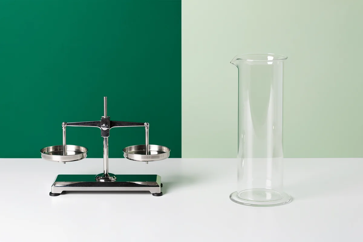 A mechanical balance and an empty glass cylinder on a white bench